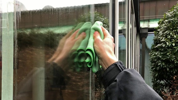 Fensterputzer Dirk Preusse putzt mit einem Mikrofasertuch ein Fenster © NDR Foto: Screenshot