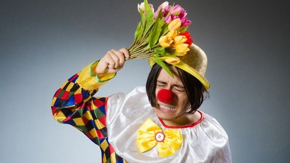 Ein Clown schlägt mit einem Strauß Tulpen auf seinen Kopf. © fotolia.com 