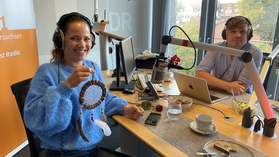 Katja Frenzel zeigt das mitgebrachte Requisit bei der Aufzeichnung des Rote Rosen Podcasts mit Host Martin Tietjen. © ARD Foto: Marlene Kukral