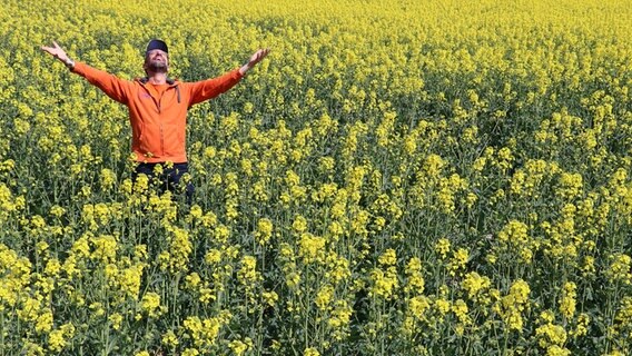 Schorse steht in einem Rapsfeld und blickt mit ausgestreckten Armen in den Himmel. © NDR Foto: Miller / Müller