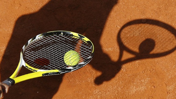 Hand mit Tennisschläger und -ball wirft Schatten auf einen Sandplatz © picture-alliance/dpa Foto: Wolfgang Kumm