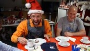 Schüssel Schorse sitzt an einem Kaffeetisch und trägt eine Weihnachtsmütze. © NDR 