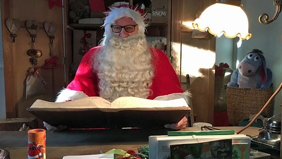 Der Weihnachtsmann sitzt an seinem Schreibtisch und schaut in ein großes Buch © NDR Foto: Hendrik Millauer