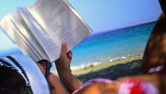 Eine Frau liegt am Strand und liest ein Buch. © picture-alliance Foto: Bildagentur Huber/G. Simeone