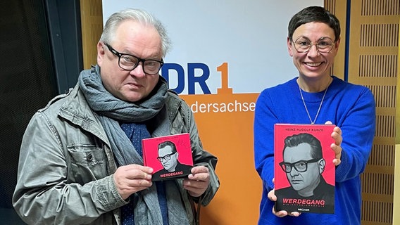 Moderatorin Martina Gilica und Heinz Rudolf Kunze halten ein handsigniertes Exemplar des Albums "Werdegang" und die Autobiografie "Werdegang" in die Kamera. © NDR 