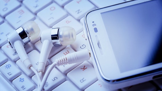 Kopfhörer mit Smartphone liegen auf einer Computertastatur. © Fotolia.com Foto: Dmytro Titov