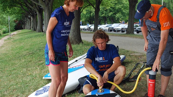 Drei Personen pumpen ein Surfbrett auf © NDR Foto: Jessi Schantin