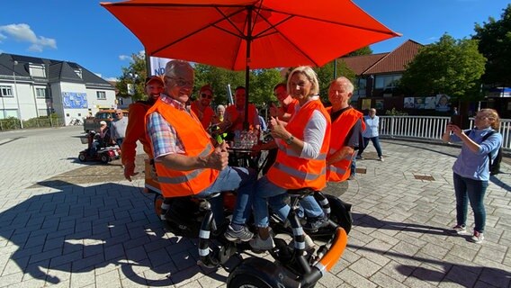 Walter Löll, Schorse, Andi Gervelmeyer, Jörg Skatulla, Erik Hauerkamp, Manfred Borsum und Monika Kallisch (v.l.) auf dem Team-Rad in Hude. © NDR Foto: Bernd Drechsler