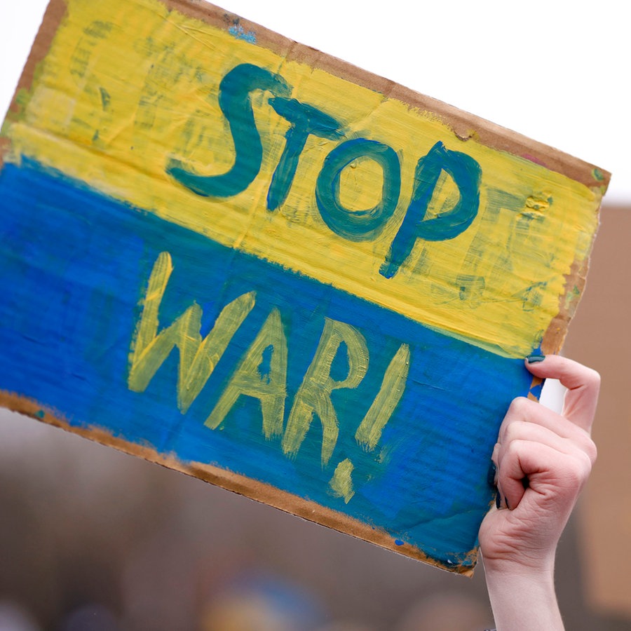 Ein Hand hält ein gelb-blaues Schild in die Luft auf dem "Stop War!" steht. © picture alliance / Geisler-Fotopress I Sebastian Gabsch/Geisler-Fotopress Foto: Sebastian Gabsch/Geisler-Fotopress