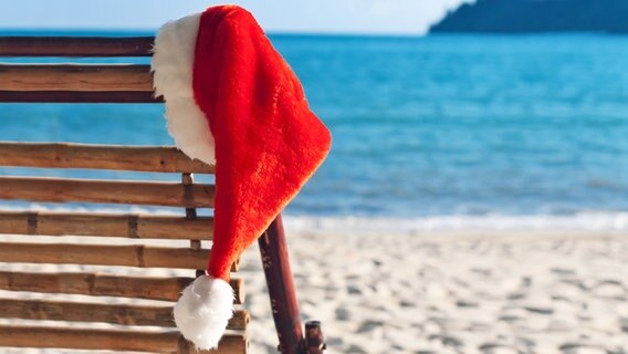 Weihnachtsmann Mütze hängt an einem Liegestuhl am Strand. © fotolia Foto: Igor Stepovik