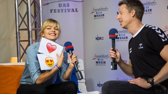 Louane hält zwei Karten mit Herz und Smiley hoch, neben ihr sitzt NDR 2 Moderator André Schünke. © NDR 2 Foto: Axel Herzig
