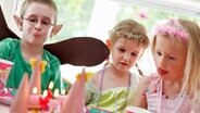 Drei Kinder sitzen an einer bunten Geburtstagstafel  