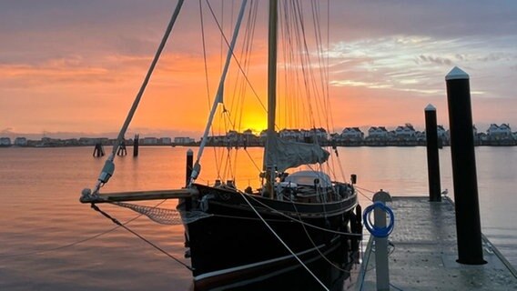 Die Sonne geht über einem kleinen Hafen auf, hüllt den Himmel in ein orange-rotes Licht. © Privat Foto: NDR 2 Hörerin Claudia