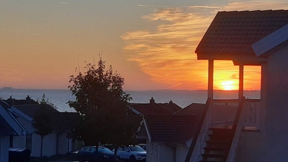 Die Sonne geht über der Lübecker Bucht bei Sierksdorf auf. Die ersten Strahlen erleuchten den Himmel orange-gold und lassen eine Siedlung erwachen. © Privat Foto: NDR 2 Hörer Michael