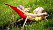 Junge Frau liegt entspannt auf einer Blumenwiese in einem Liegestuhl © Fotolia.com Foto: Almgren