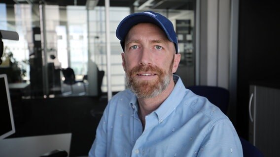 Jan Kuhlmann aus der NDR 2 Musikredaktion sitzt in seinem Büro am Schreibtisch und lächelt in die Kamera.  Foto: Marek Nowacki