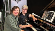 Stefanie Hempel und Angela Gobelin sitzen an einem Klavier, mit Büchern über Joni Mitchell. © Stefanie Hempel 