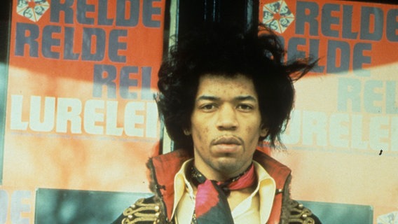 Der Gitarrist Jimi Hendrix steht vor Plakaten © picture alliance / Photoshot 