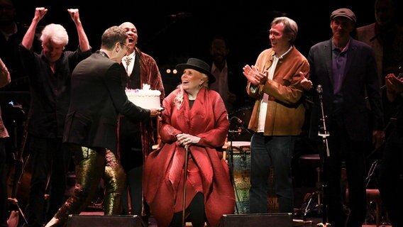 Die Musikerin Joni Mitchell bekommt bei der Veranstaltung "Joni 75: A Birthday Celebration" auf der Bühne einen Kuchen zu ihrem 75. Geburtstag gereicht. © picture alliance/AP Photo Foto: picture alliance/AP Photo