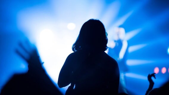 Das Publikum bei einem Konzert als Silhouette, von vorne angestrahlt von blauem Licht. © IMAGO / agefotostock 
