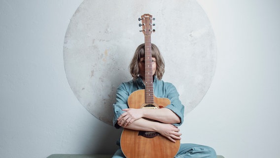 Die Musikerin Teresa Bergmann sitzt mit einer Gitarre vor einer Wand. © Zachow Pictures 