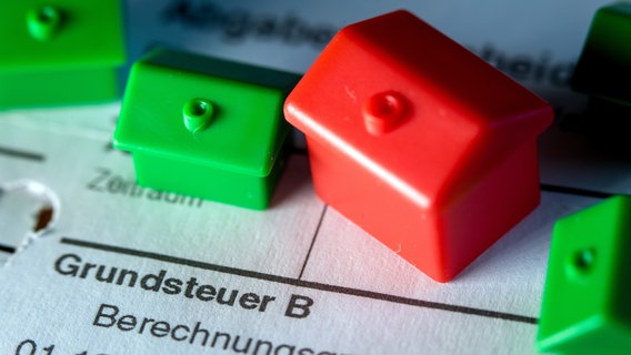 Kleine Spielzeughäuser aus Kunststoff stehen auf einem Abgabenbescheid für die Entrichtung der Grundsteuer. In die zähen Verhandlungen von Bund und Ländern über eine Reform der Grundsteuer hat Schleswig-Holstein einen neuen Kompromissvorschlag eingebracht. © picture alliance/dpa | Jens Büttner Foto: picture alliance/dpa | Jens Büttner