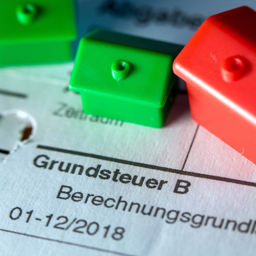 Kleine Spielzeughäuser aus Kunststoff stehen auf einem Abgabenbescheid für die Entrichtung der Grundsteuer. In die zähen Verhandlungen von Bund und Ländern über eine Reform der Grundsteuer hat Schleswig-Holstein einen neuen Kompromissvorschlag eingebracht. © picture alliance/dpa | Jens Büttner Foto: picture alliance/dpa | Jens Büttner