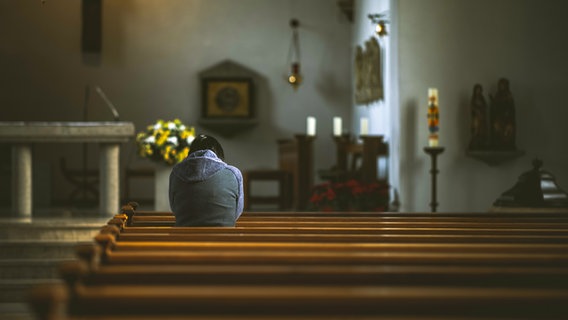 Eine Person steht in einer ansonsten leeren Kirchenbank © photocase David W. Foto: David W.