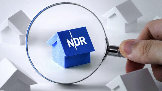 Eine Lupe deutet auf ein blaues Papierhäuschen mit dem Logo des NDR auf dem Dach, das zwischen anderen weißen Papierhäuschen steht. © fotolia.com Foto: Kenishirotie