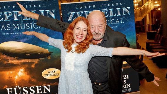 Ralph Siegel und Ehefrau Laura Siegel posieren vor Plakaten zum Musical "Zeppelin" von Ralph Siegel. © Goran - Nitschke Foto: Walter Wicha
