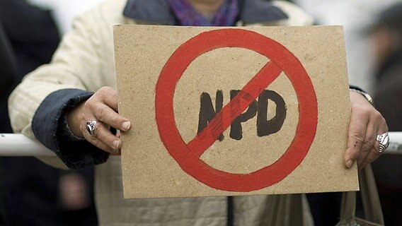 Eine Demonstrantin hält ein Pappschild, auf dem Die Buchstaben NPD durchgestrichen sind. © Imago/IPON 