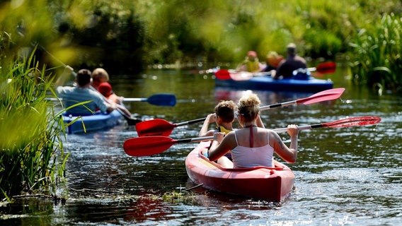 Wassersportler sitzen in ihren Kanus und Booten auf dem Wasser und halten die Paddel waagerecht.  