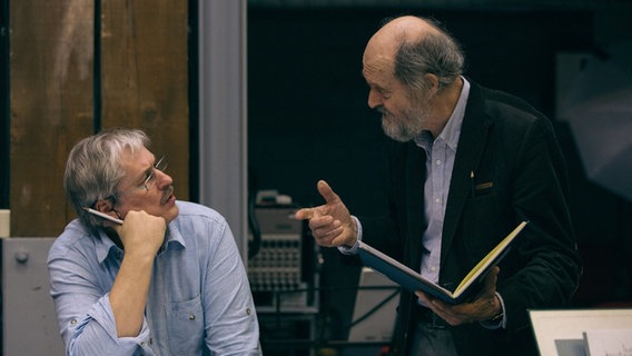 Zwei Männer über aufgeklappten Notenbüchern ins Gespräch vertieft: Links sitzend Sigvards Kļava, rechts stehend Arvo Pärt. Zwei Männer über aufgeklappten Notenbüchern ins Gespräch vertieft: Links sitzend Sigvards Kļava, rechts stehend Arvo Pärt. © Latvian Radio Choir