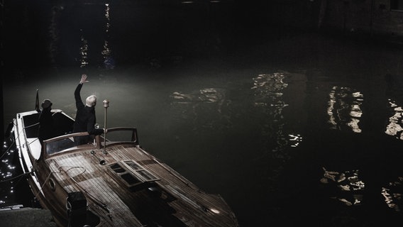 Screenshot: Zwei Schauspieler stehen im Film"Cinephonie Noir" winkend auf einem Boot. © NDR Bigband Foto: Screenshot