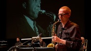 Screenshot: Ein Musiker der NDR Bigband spielt Saxofon, im Hintergrund eine Leinwand mit Charlie Parker. © NDR Foto: Screenshot