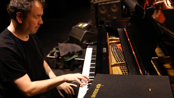 Pianist Florian Weber bei der Probe. Auf dem aufgeklappten Flügel liegt eine schwarze Notenmappe mit goldenen Lettern, in denen "NDR Bigband" zu lesen ist. © NDR Foto: Ed Satterwhite