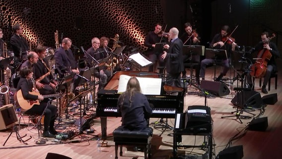 Konzertszene: Die NDR Bigband und das Atom String Quartet gemeinsam mit Geir Lysne und Pianist Vladyslav Sendecki auf der Bühne der Elbphilharmonie Hamburg (Screenshot © NDR Foto: Screenshot