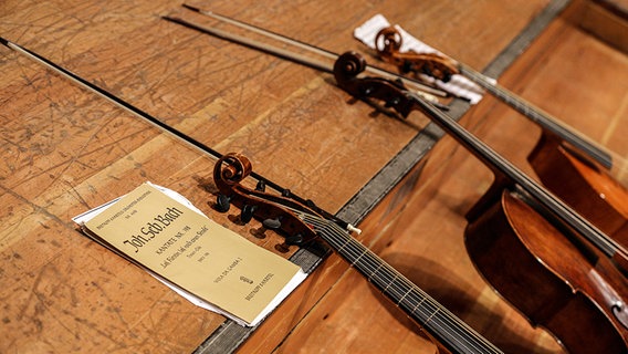 Celli und Bögen liegen angelehnt an ein Bühnenpodium in der Laeiszhalle. Im Vordergrund: die Partitur einer Bachkantate.  Foto: Marcus Krüger