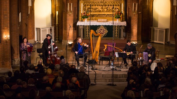 Fünf Musiker sitzen mit Instrumenten wie Harfe, Kontrabass und Gitarre im Altarraum einer Kirche. © NDR Foto: Axel Herzig