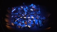 Aufsicht: das Andromeda Mega Express Orchestra von oben auf einer bläulich beleuchteten Bühne © Andromeda Mega Express Orchestra 