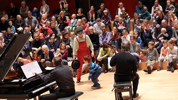 Konzertszene: Christof Hahn (Klavier), Sven Forsberg (Cello) und Christina Dean (in roten Latzhosen) gemeinsam mit den Kindern und ihren Familien Konzertszene: Christof Hahn (Klavier), Sven Forsberg (Cello) und Christina Dean (in roten Latzhosen) gemeinsam mit den Kindern und ihren Familien © NDR Foto: Marcus Krüger