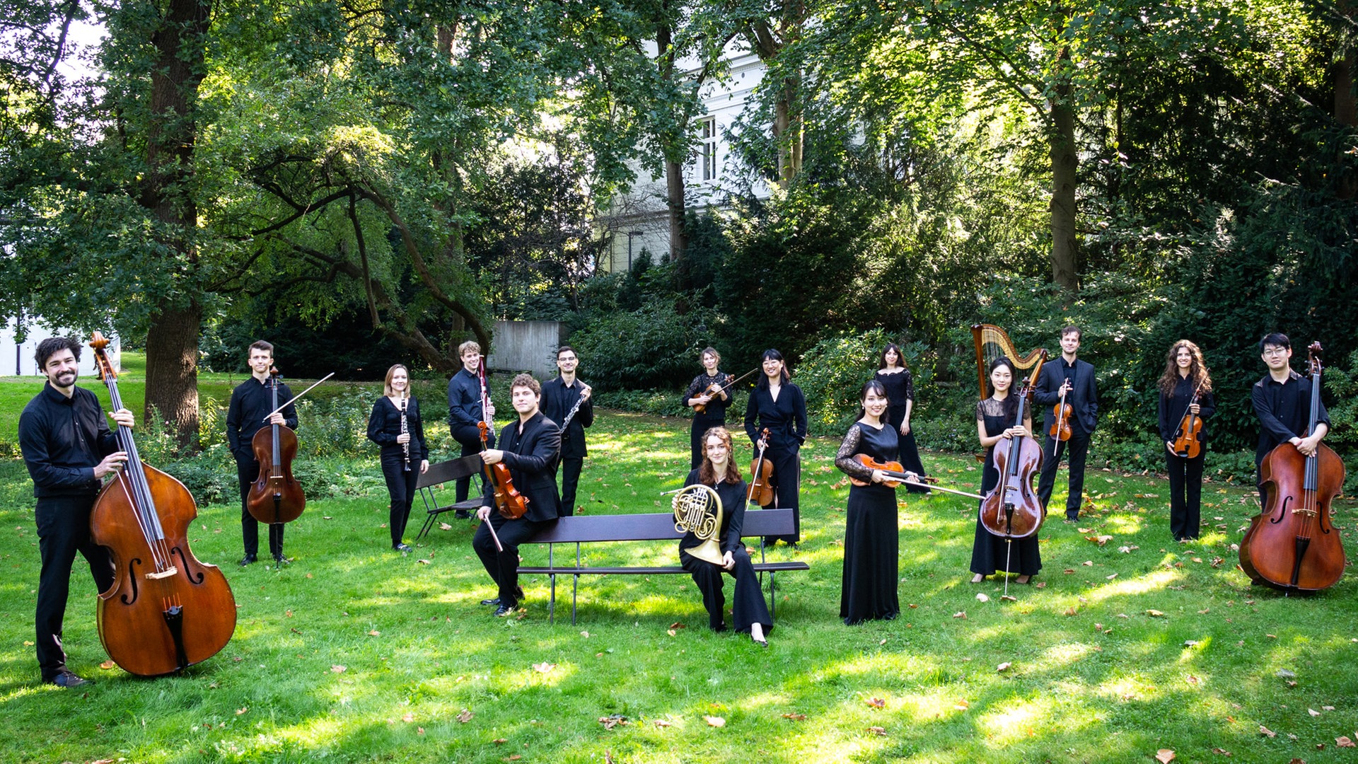 Stipendiatinnen und Stipendiaten der Akademie des NDR Elbphilharmonie Orchesters stehen mit ihren Instrumenten in einem Garten. © NDR 