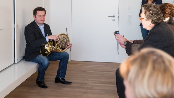 Dave Claessen wird mit seinem Instrument in der Hand im Stimmzimmer der Hornisten in der Elbphilharmonie von Journalisten fotografiert. © NDR Foto: Axel Herzig