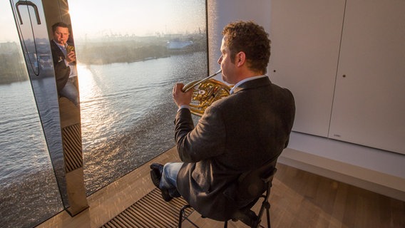 Dave Claessen hornspielend vor dem Fenster des Hornstimmzimmers mit Blick auf die Elbe © NDR Foto: Axel Herzig