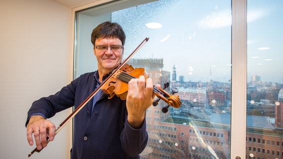 Konzertmeister Stefan Wagner mit seiner Geige im Stimmzimmer in der Elbphilharmonie. Hinter ihm der Ausblick auf den Michel. © NDR Foto: Axel Herzig