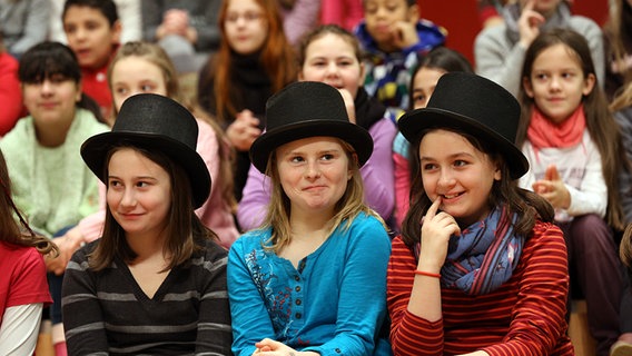 Kinder im Publikum. In der ersten Reihe sitzen drei Mädchen mit schwarzen Zylindern auf dem Kopf. © NDR Foto: Marcus Krüger