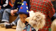 Kind mit Pulcinella-Hut läßt sich von Handpuppe Bodo etwas ins Ohr flüstern © NDR Foto: Marcus Krüger