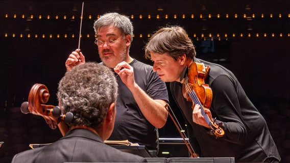 Dirigent Alan Gilbert und Violinst Joshua Bell schauen gemeinsam in die Partitur auf der Bühne in der Alten Oper Frankfurt. © NDR Foto: Daniel Tomann-Eickhoff