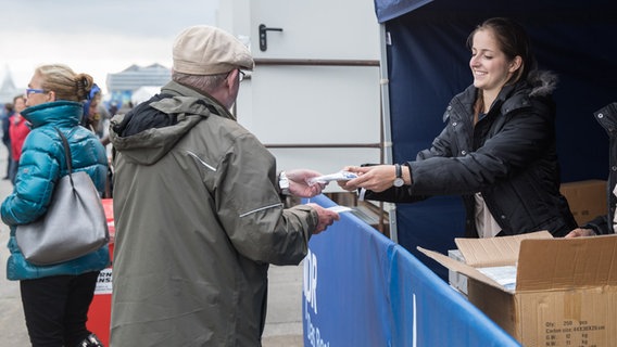 Beim HafenCity Open Air 2016: Ein Besucher bekommt ein verpacktes Regencape von einer jungen Frau überreicht. © NDR Foto: Axel Herzig