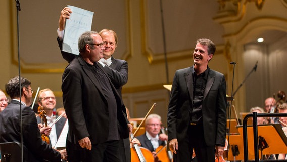 Applaus für Komponist Marc-André Dabalvie (dem Thomas Hengelbrock seine Partitur über den Kopf hält), Dirigent Hengelbrock und Countertenor Philippe Jaroussky © NDR Foto: Axel Herzig